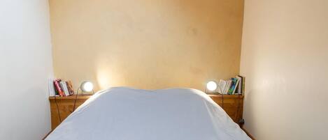 A narrow room with a bed, two bedside tables with lamps, and bookshelves.