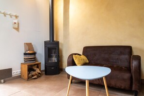 Ein Wohnzimmer mit einer braunen Ledersofa, einem blauen Tisch, einem schwarzen Holzofen und einem Holztisch mit einem gewebten Korb.