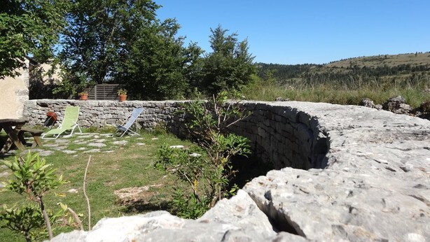 Ein Steinbauwerk mit einer Rasenfläche, einer Steinmauer und Bäumen im Hintergrund.