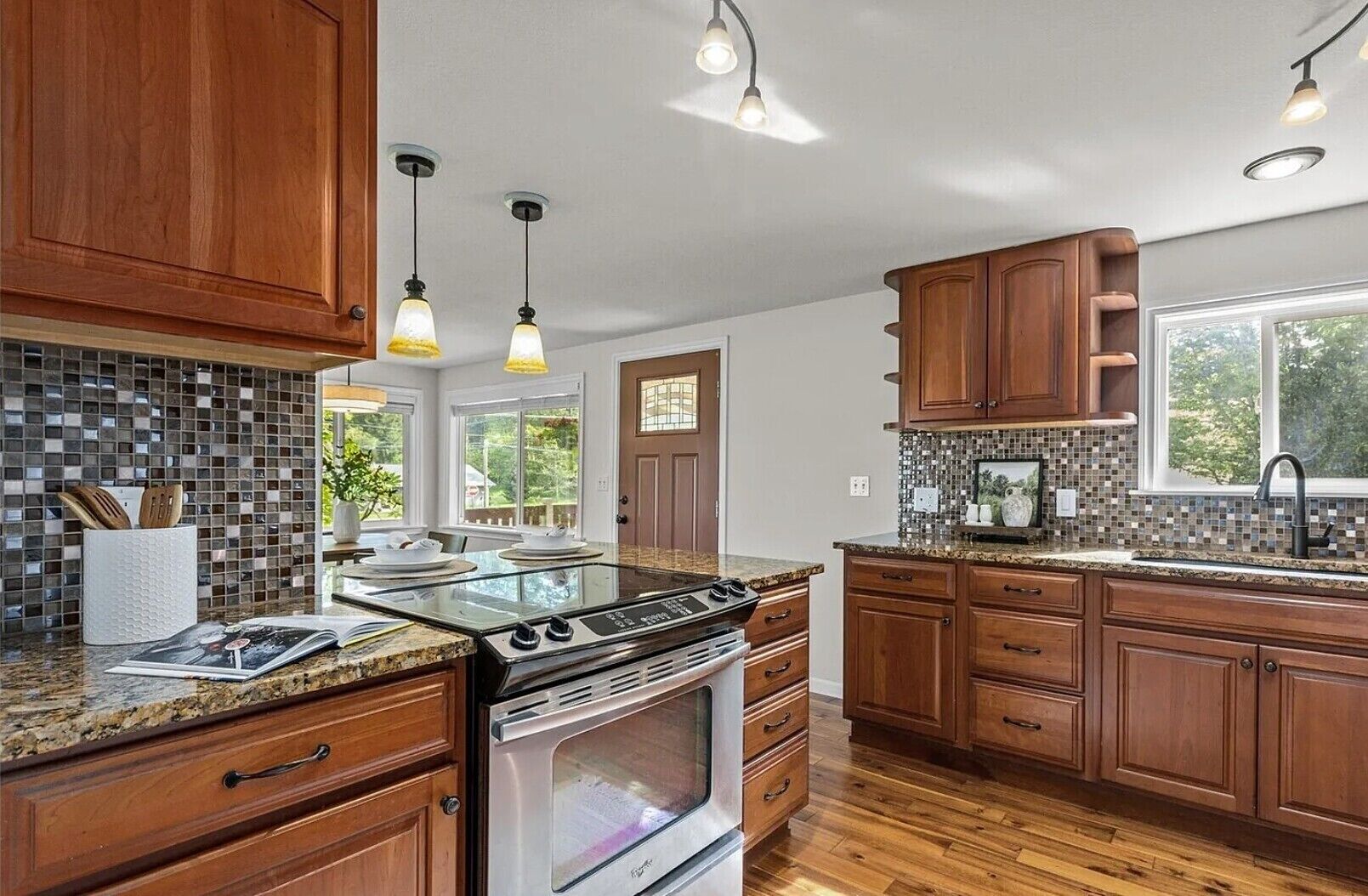 A kitchen with wooden cabinets, a granite countertop, a stainless steel stove, and pendant lighting.