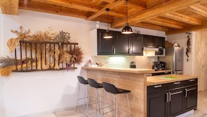 Una cocina con techo de madera, armarios negros, encimera de madera y tres taburetes de bar.