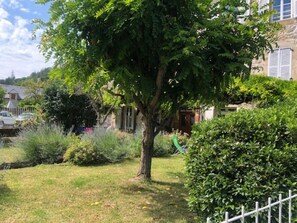 A residential garden with a large tree, a hedge, and a white fence. - La Glycine 5/6 persons (LA CANOURGUE)