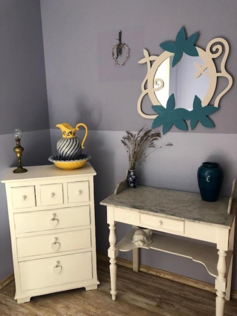 A white dresser with drawers, a small table with a vase, and a wall-mounted mirror.