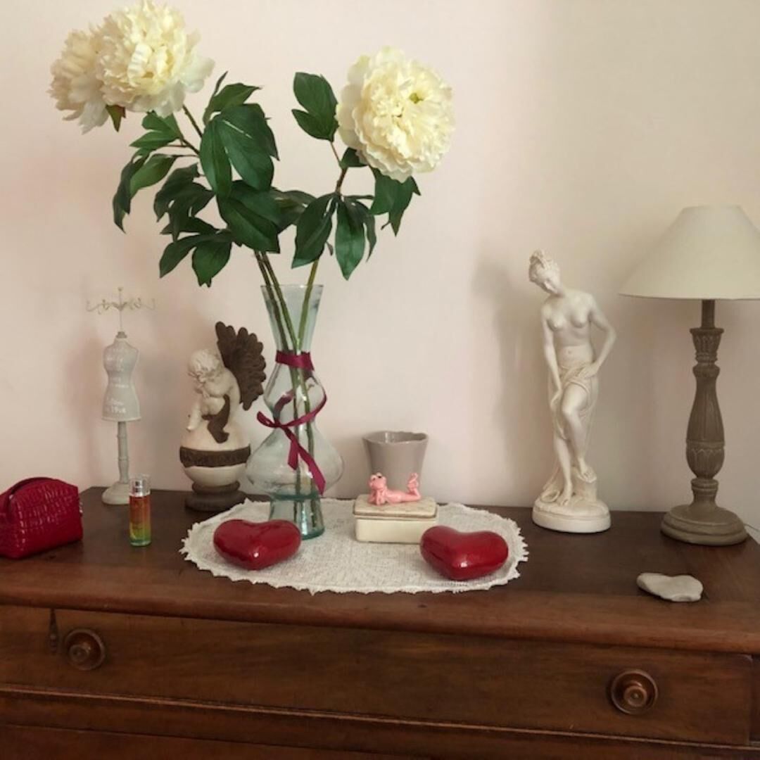 Ein hölzerner Kommode mit einer Vase voller weißer Blumen, einer kleinen Figur, einer Lampe und einer Statue.