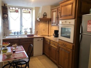 A kitchen with wooden cabinets, a dishwasher, an oven, and a refrigerator. - La Glycine 5/6 persons (LA CANOURGUE)