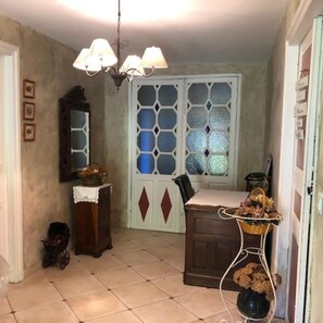 Una stanza con pavimento piastrellato, una panca in legno, un armadietto bianco, uno specchio, una finestra con vetri decorati e un lampadario.