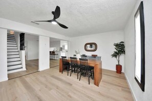 Ein modernes Interieur mit Essbereich, Deckenventilator, Treppe und einer Küche im Hintergrund.