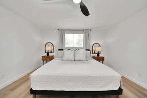 Ein Schlafzimmer mit einem Bett, einem Deckenventilator, einem Fenster mit Vorhängen und Nachttischlampen.