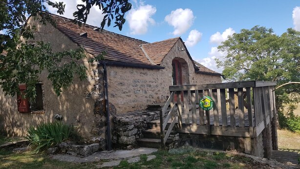 Een landelijk stenen gebouw met een pannendak, een houten trap en een bordje dat aangeeft dat het deel uitmaakt van het 'Gites de France' netwerk.