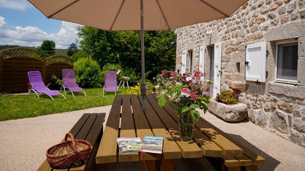 Een houten tafel met een beige parasol, een rieten mand en een vaas met bloemen.