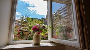 Een uitzicht op een tuin en een stenen muur vanuit een raam.