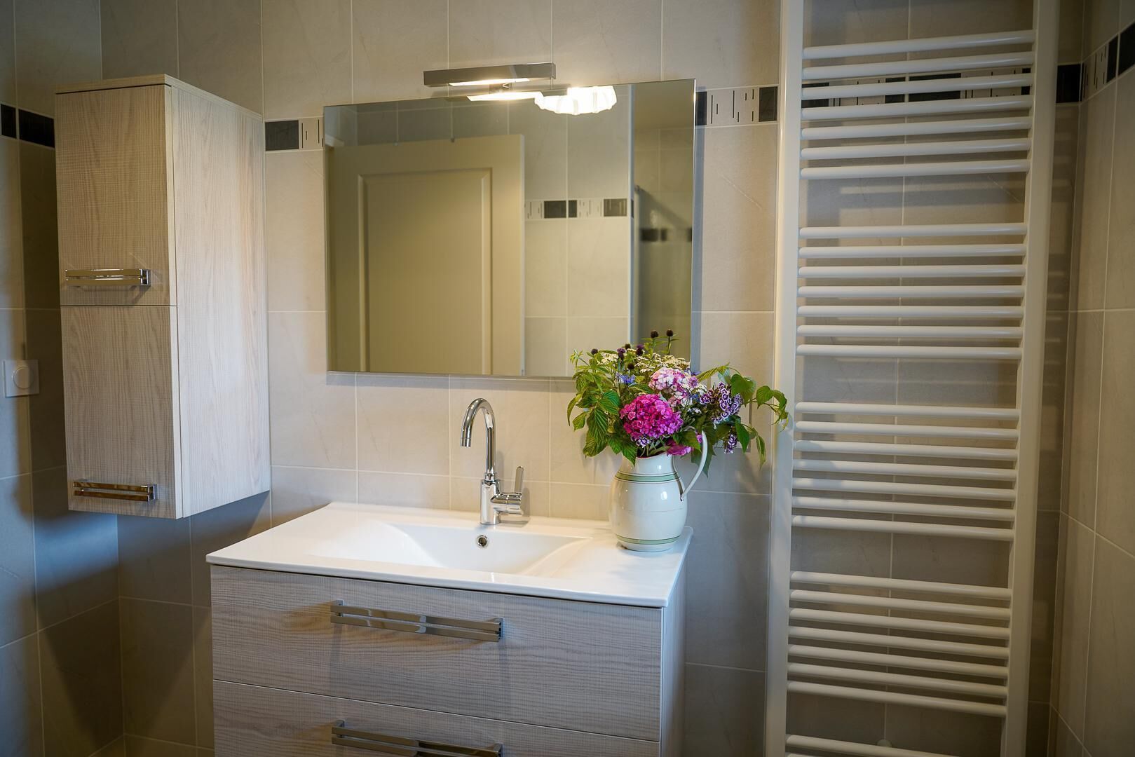 Een moderne badkamer met een witte wastafel, een spiegel, een kast en een handdoekhouder.