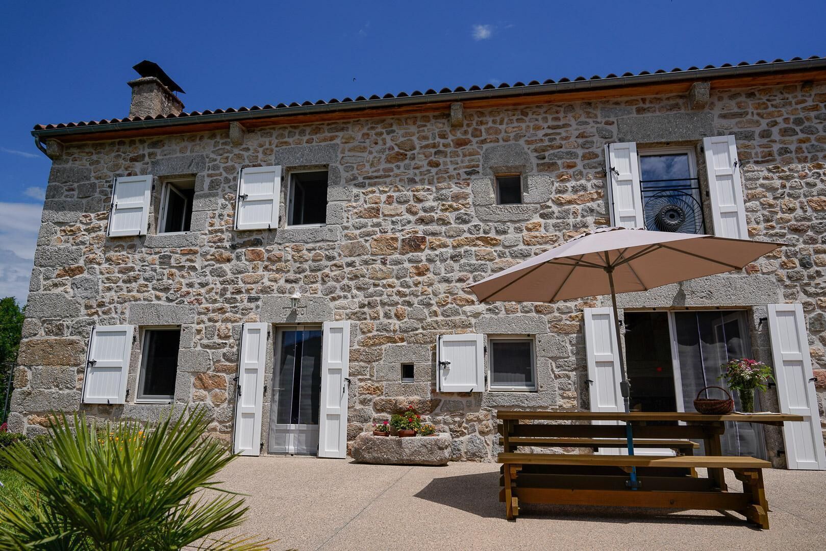 A stone building with multiple windows, a wooden bench, and a large umbrella.