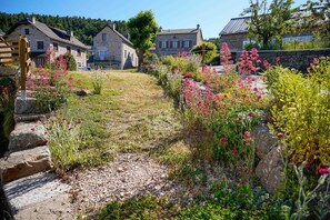 Ein Steinhäuschen mit Holzzaun, umgeben von einem Garten mit verschiedenen Pflanzen und Blumen.