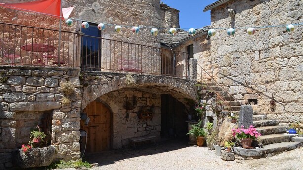 Un edificio de piedra con puerta de madera, un pequeño balcón con barandilla metálica y una escalera de piedra que sube a un nivel superior.