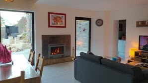 A living room with a fireplace, a sofa, a dining table with chairs, and a television. - La Cazelle - LE ROZIER (LE ROZIER)
