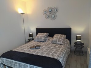 A neatly made bed with patterned bedding, two bedside lamps, a decorative wall piece, and a book on the bed. - La Cazelle - LE ROZIER (LE ROZIER)
