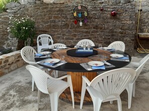 A round wooden table with white plastic chairs, surrounded by a stone wall with a fire extinguisher and a water hose. - La Cazelle - LE ROZIER (LE ROZIER)