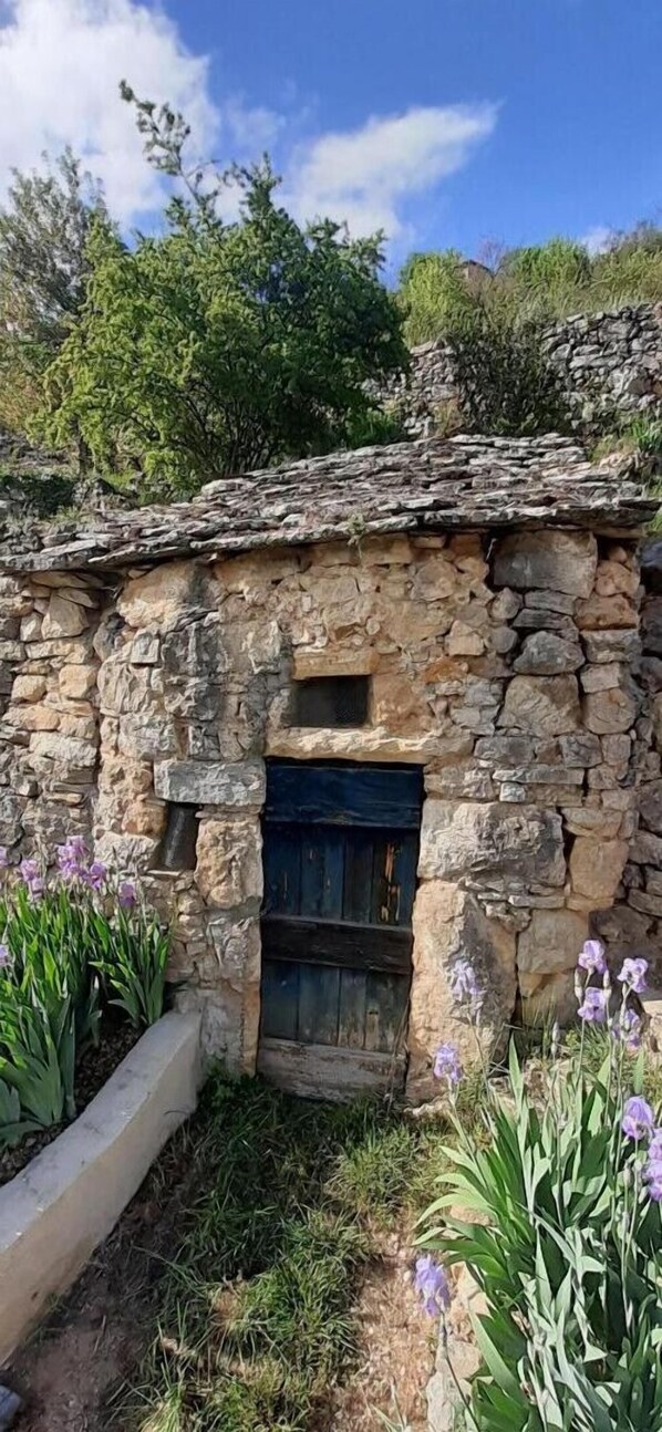 Ein Steinhaus mit Holztür, umgeben von viel Grün und Blumen.