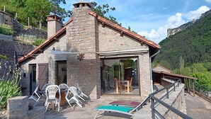 A stone building with a tiled roof, a glass door entrance, and a patio with chairs and a table. - La Cazelle - LE ROZIER (LE ROZIER)