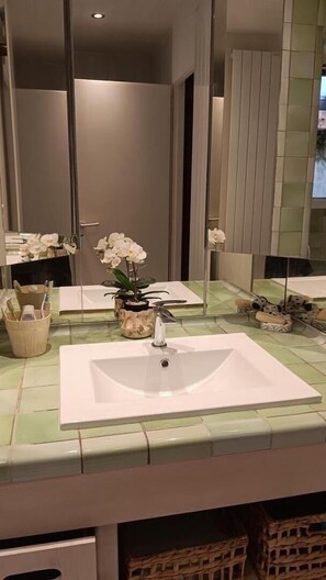 A bathroom with a large mirror, white sink, and decorative items including orchids. - La Cazelle - LE ROZIER (LE ROZIER)