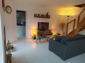 Ein Wohnzimmer mit einer Couch, Fernseher, Lampe und einer Treppe.
