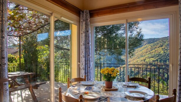 A dining area with a table set for two, overlooking a mountainous landscape. - Les Hauts de Maison Rouge (VIALAS)