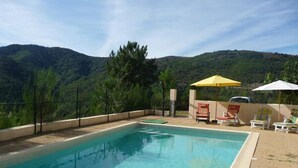 A swimming pool with lounge chairs and umbrellas, surrounded by a fence and greenery. - Les Hauts de Maison Rouge (VIALAS)