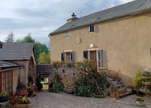 A stone building with a tiled roof, a small entrance, and a garden with potted plants and flowers. - Gache's House - LA CANOURGUE (LA CANOURGUE)
