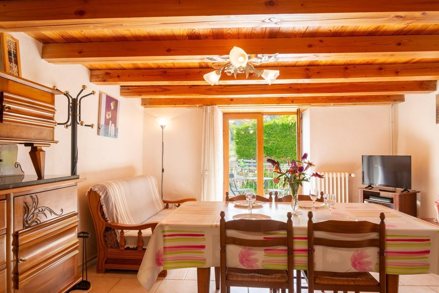 Interior em madeira com mesa de jantar, cadeiras, sofá, televisão e janela com vista para o verde.