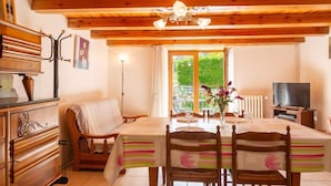 Een houten interieur met een eettafel, stoelen, een bank, een televisie en een raam met uitzicht op groen.