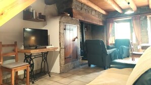 A rustic interior with a stone fireplace, wooden beams, a television on a table, and a sofa. - LA DROSERA - LAJO - Gîte (LAJO)