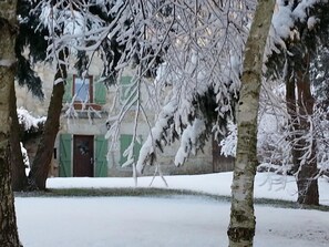 Schneebedeckte Landschaft mit Bäumen und einem Gebäude mit grünen Fensterläden.