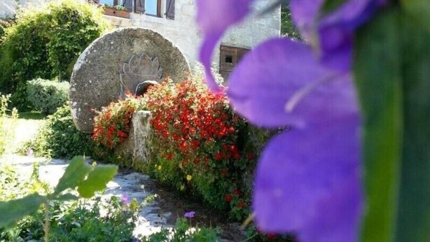 A stone building with a rustic charm, a stone archway, and a variety of colorful flowers in the foreground. - LA DROSERA - LAJO - Gîte (LAJO)