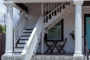 Eine Treppe mit weißen Geländern führt zu einem Veranda-Bereich mit Tisch und Stühlen.