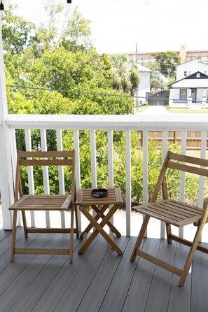 Eine Holzterrasse mit zwei Stühlen und einem kleinen Tisch, mit Blick auf eine grüne Landschaft und Wohnhäuser.