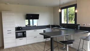 Een moderne keuken met een centraal kookeiland, barkrukken, een flatscreen televisie en een groot raam.
