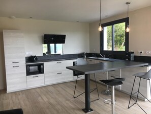 Una cocina moderna con una isla central, taburetes de bar, un televisor de pantalla plana y un ventanal grande.