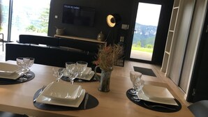 Een moderne eethoek met een houten tafel voor vier personen, een aan de muur bevestigde televisie en uitzicht op bergen.