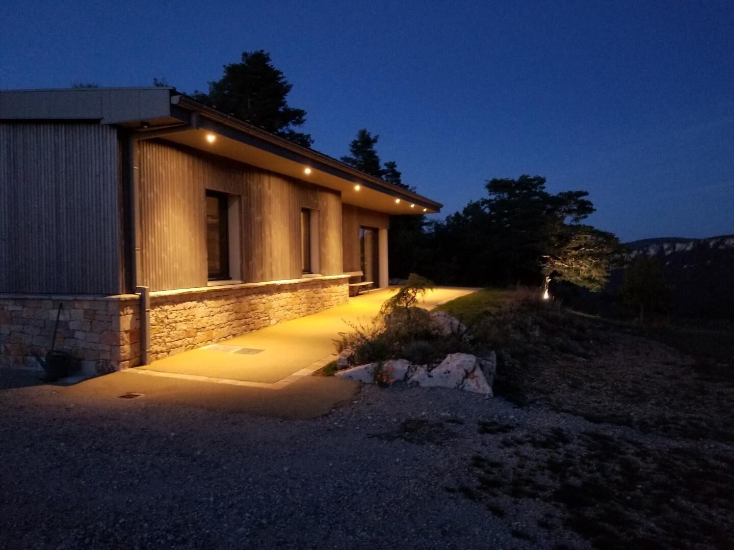 A modern house with a stone foundation, a wooden exterior, and a well-lit entrance.