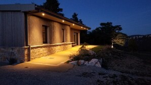 Een modern huis met een stenen fundering, een houten gevel en een goed verlichte entree.