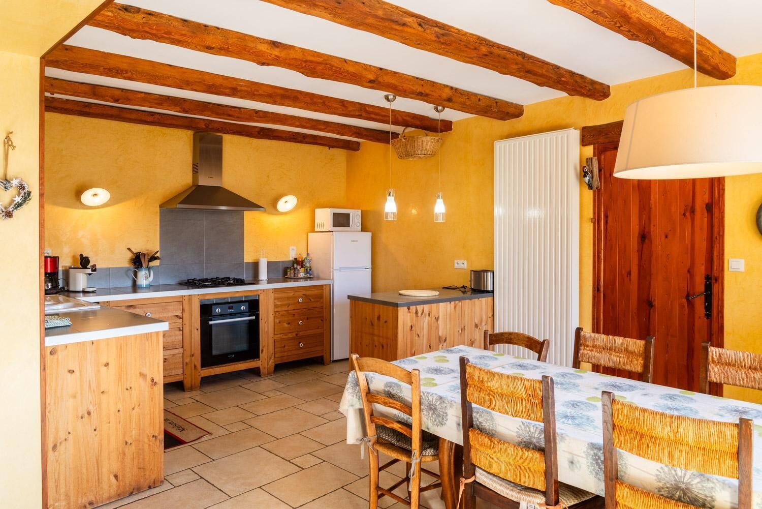 Une cuisine avec des poutres en bois, une table à manger avec des chaises, un réfrigérateur et un four à micro-ondes.