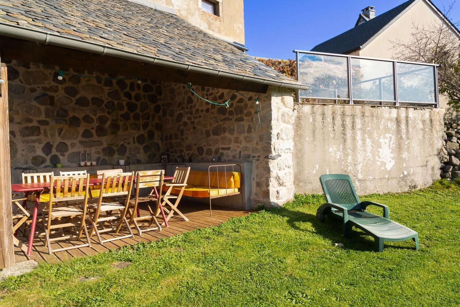 A stone building with a wooden deck, outdoor seating, and a glass window overlooking a landscape.