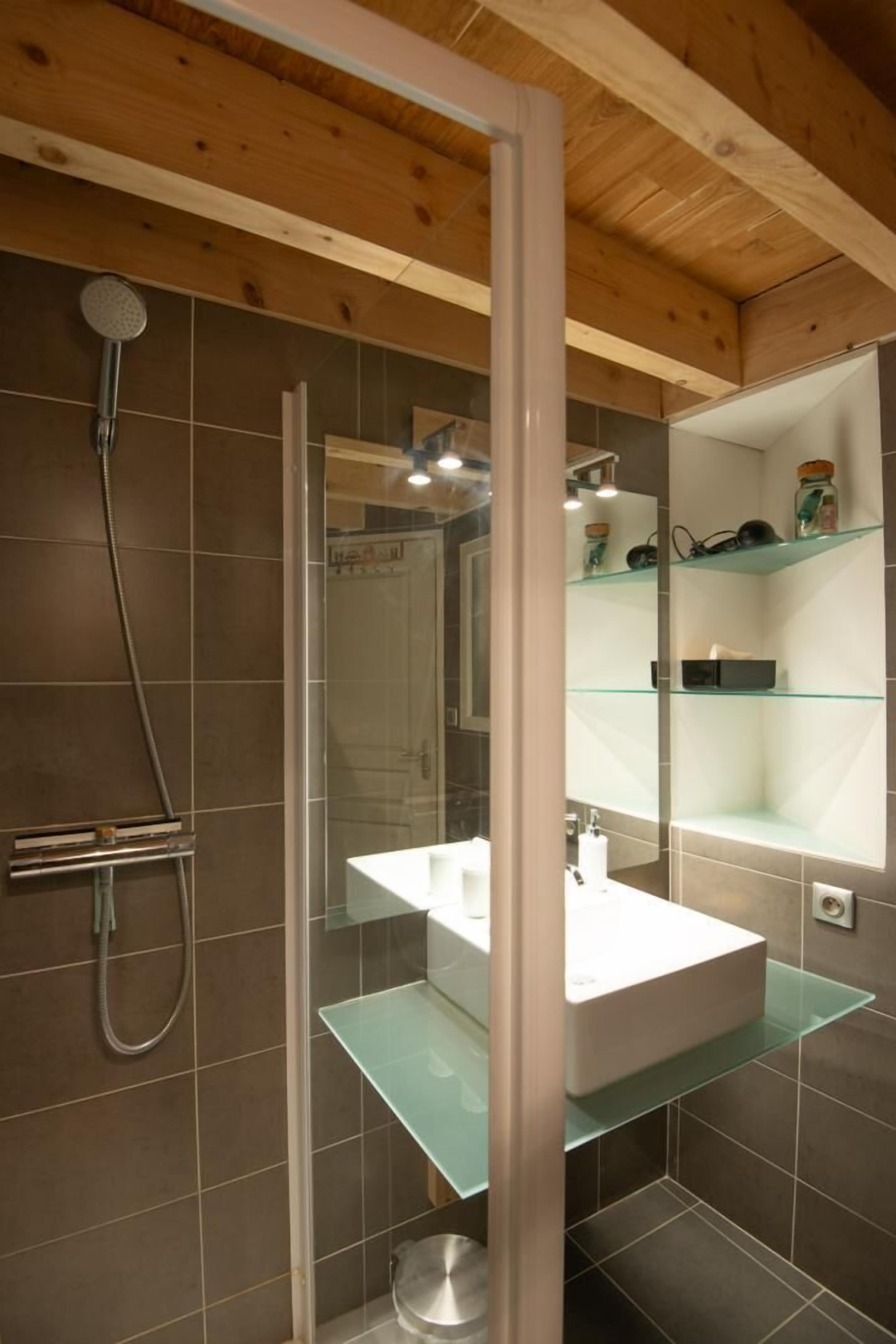 Une salle de bain moderne avec une douche à parois de verre, un lavabo blanc et des étagères en verre.