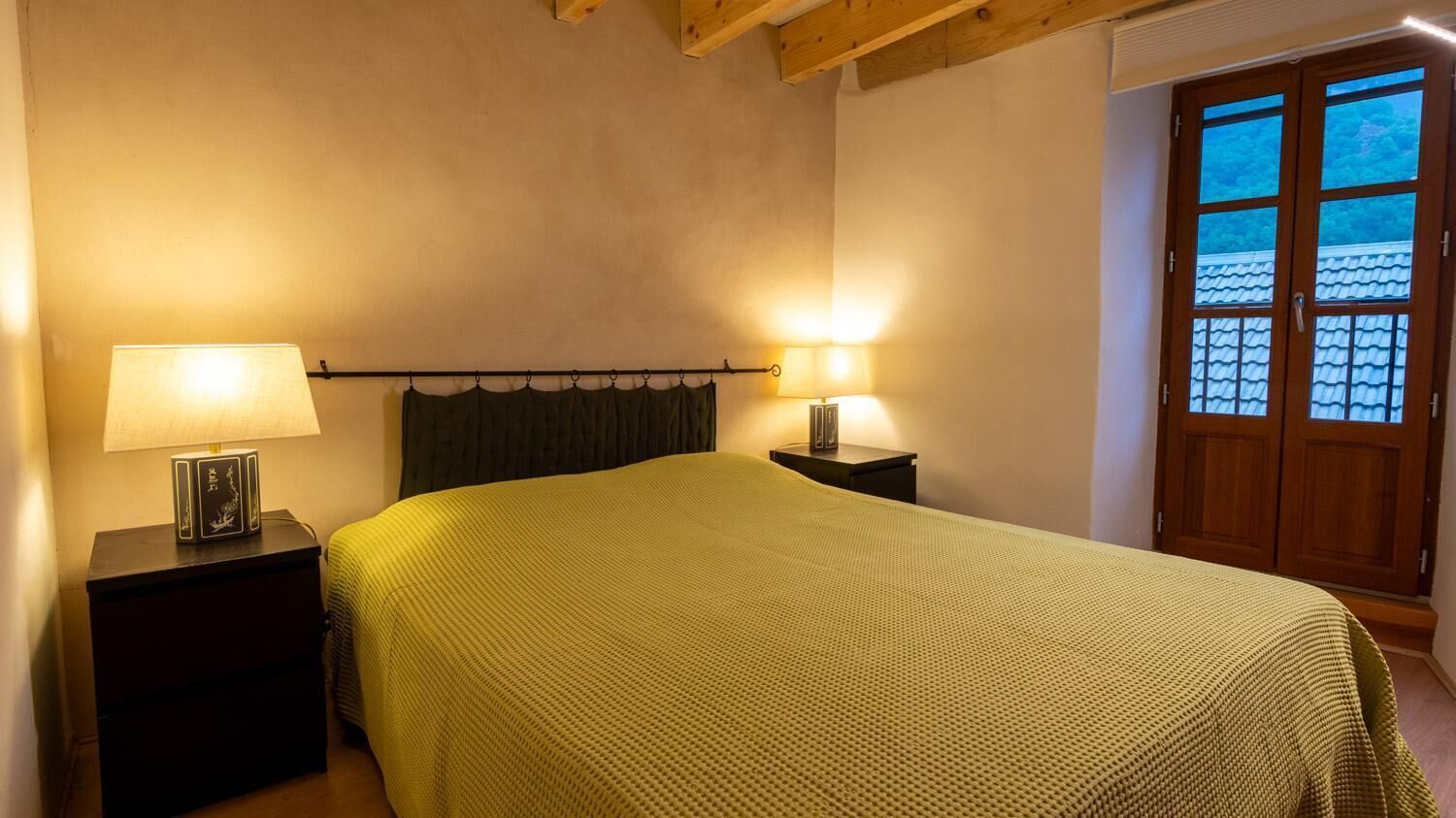 Une chambre avec un lit, deux lampes de chevet, une tête de lit sombre et une porte en bois avec des panneaux de verre.