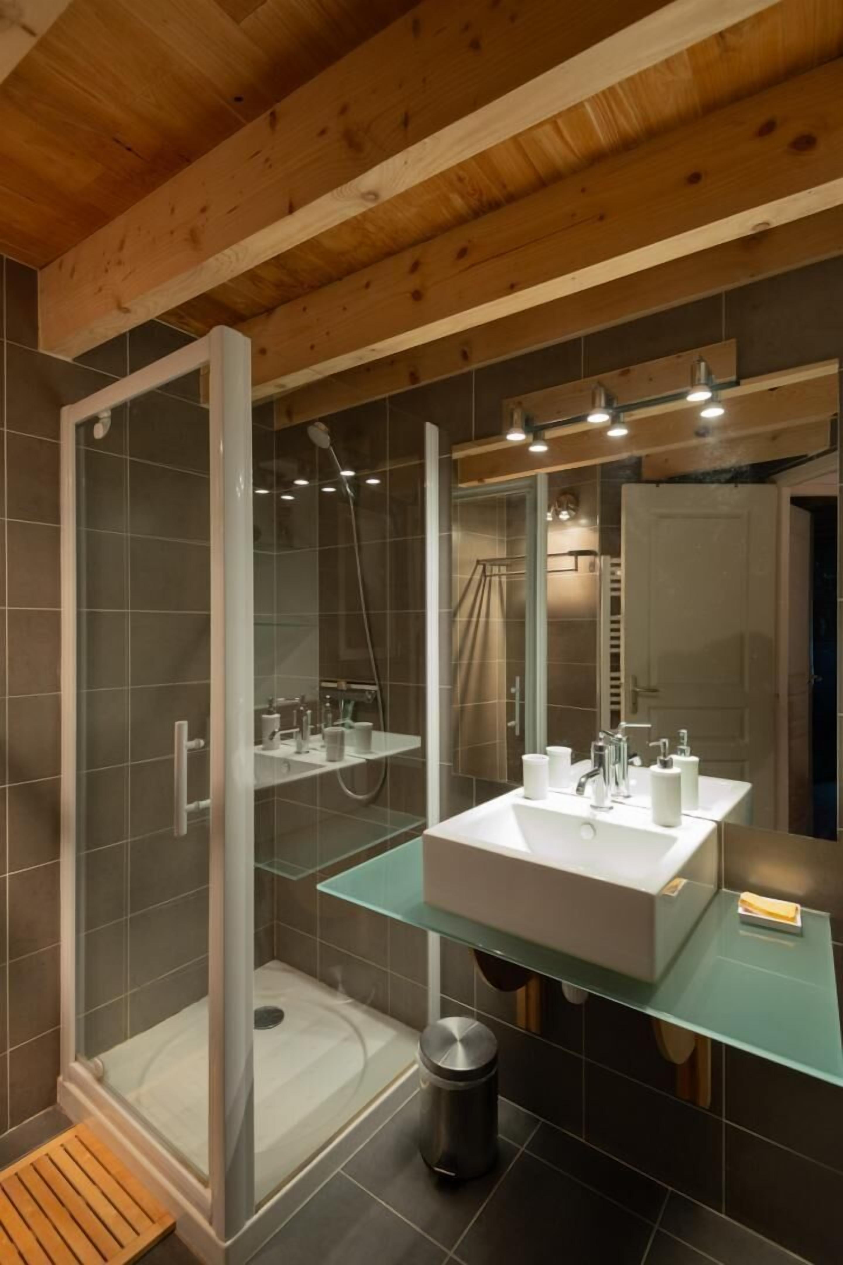 Un baño moderno con cabina de ducha de vidrio, un lavabo blanco y encimera de vidrio.