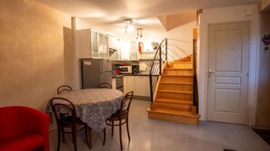 Eine kleine Küche mit Esstisch, Stühlen, einem Kühlschrank, einer Mikrowelle und einer Holztreppe.