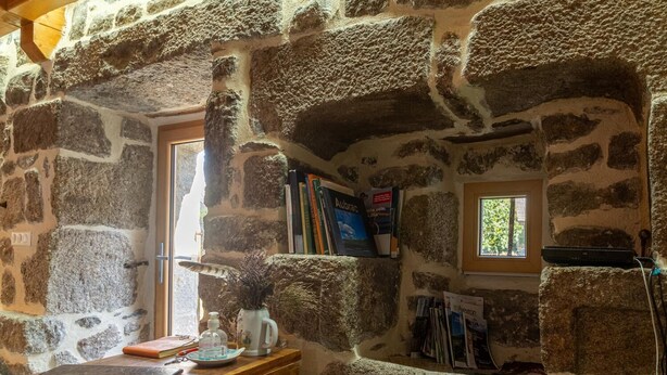 Ein Zimmer mit Stehwänden, einem Holztisch, einem Fenster und einem Bücherregal.