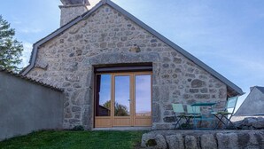 Ein Steinhaus mit einer großen Holztür und einer kleinen Terrasse mit Klappstühlen.