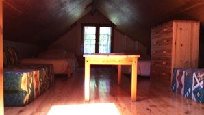 Een zolderkamer met een houten tafel, een kapstok en een bed.